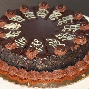 The GD-018 Chocolate Decadence Gluten Free cake is round with glossy ganache, piped chocolate decorations, white chocolate swirls on top, and sits on a gold board with piped chocolate frosting around the base.