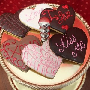 CE-020a Valentine's: Heart-shaped cookies with chocolate and icing, featuring messages like Love, Kiss Me, and XOXO, arranged on a tiered platter against a red polka dot background.