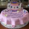 The CB-028D is a round cake with pink fondant, "Happy 5th Birthday Daniella" in purple icing, plus paper teapot and teacups, and pastel fondant flowers as decorations.