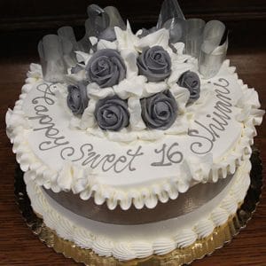 The AN-003 is a round cake with white icing, gray and white fondant roses, "Happy Sweet 16 Shivani" written on top, decorative ribbon accents, and presented on a gold tray.