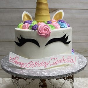 The CB-021B is a unicorn-themed birthday cake featuring a gold horn, white ears, pastel flowers, black eyelash decorations, and displayed with a "Happy Birthday Isabella!" sign.