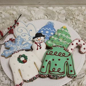 A plate of CE-100b Assorted chocolate dipped Christmas cookies, featuring sweaters, a tree, snowflakes, a candy cane, and a snowman, artistically arranged with festive accents.