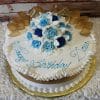 The AN-005 is a round white birthday cake with blue and white icing roses, gold ribbon accents, and "Happy Birthday Dana" in blue script. The cake is presented on a gold board.