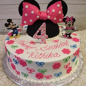 The CB-001A is a round birthday cake featuring Minnie Mouse ears, a pink polka dot bow, colorful flowers and bows, and Minnie and Mickey Mouse figures. “Happy Birthday Rithika” and a pink polka dot number 4 are on top.
