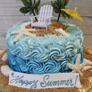 The BD-137 is a beach-themed cake featuring blue swirled frosting, white starfish, edible sand, palm trees, a mini white chair and yellow umbrella, plus a “Happy Summer!” sign on the front.
