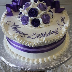 The AN-007 is a round white cake topped with purple and white roses, a purple ribbon, and "Happy Birthday Love" in purple icing. Presented on a silver platter.