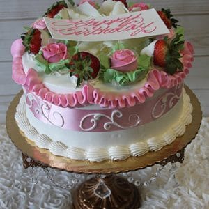 The AN-001 birthday cake features white and pink frosting, strawberries, pink roses, and green leaves atop a gold cake stand. A white plaque with "Happy Birthday" in pink decorates the top.