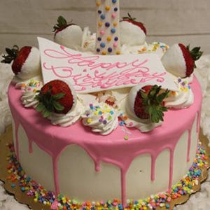 The CB-023D is a round cake with white frosting, pink drip icing, a large 1 candle, chocolate-covered strawberries, whipped cream swirls, colorful sprinkles, and a Happy Birthday card on top.