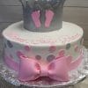 The BB-028 cake is round with pink and gray polka dots, a pink bow, a silver crown topper with pink baby footprints, and pink script text on the top edge. It sits on a silver board.