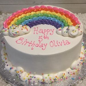 The CB-022A is a round white birthday cake topped with an icing rainbow and clouds, decorated with sprinkles, and features "Happy 5th Birthday Olivia" in pink lettering.