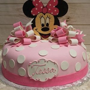 CB-001C is a round pink cake with white polka dots, fondant bows, and a large Minnie Mouse face topper. It features a white plaque with "Tessa" written in cursive.
