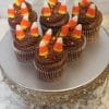 Seven CC-054 Mini Halloween cupcakes—chocolate with white mousse filling—each topped with three candy corn pieces, are displayed on a silver decorative cake stand.