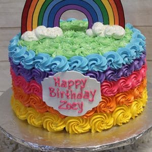 The CB-022B is a colorful birthday cake with rainbow-striped frosting, topped with a paper rainbow and clouds, featuring a "Happy Birthday Zoey" plaque on a silver-covered board.