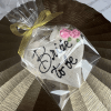 The CE-003h bridal cookie is heart-shaped, decorated with pink roses and "Bride to be" in black icing, wrapped in clear plastic with a gold ribbon, and displayed on a shiny textured gold surface.