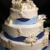 The WD-053 is a three-tiered white cake adorned with sea-themed fondant, featuring seahorses, seashells, coral accents, and blue wave bands around each tier.