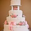 The WD-138 is a four-tiered white wedding cake adorned with pink fondant bows, roses, green leaves, and ornate white icing details, presented on a silver cake board.