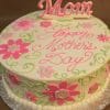 The MD-020 is a round cake with white icing, pink and green floral designs, "Happy Mothers Day" written in pink, and a pink "Mom" topper.